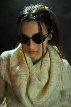 Stylish portrait of a woman in a white sweater and sunglasses against a dark background.