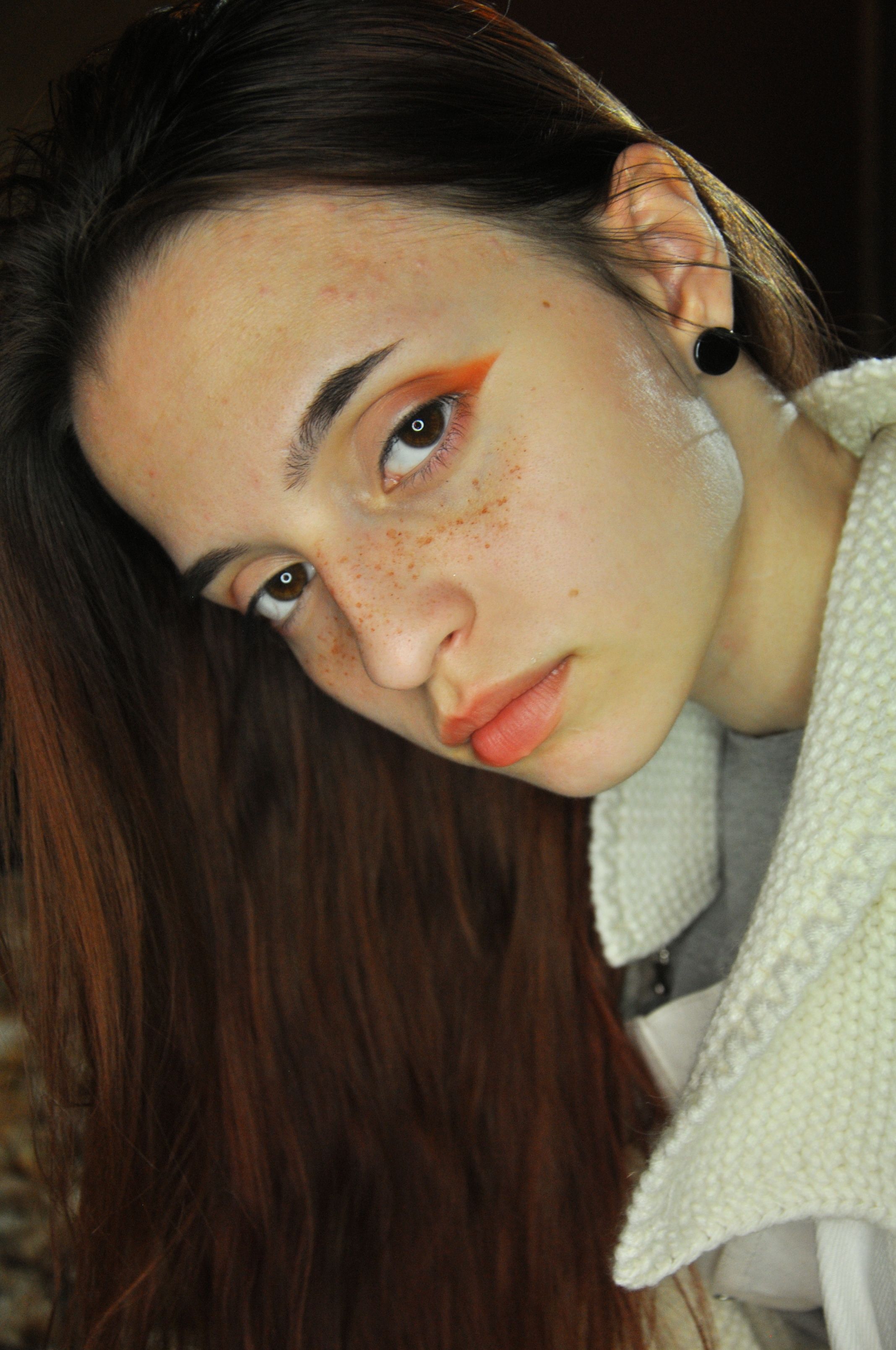 A close-up portrait of a young woman with striking makeup and a contemplative expression.