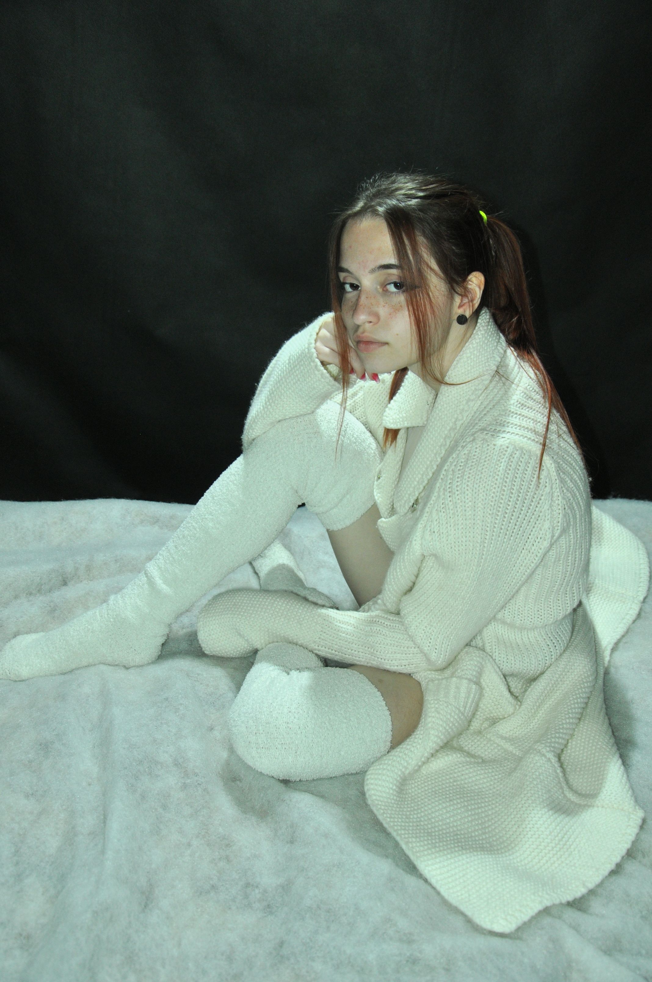 A serene portrait of a woman in white knitwear, exuding warmth and relaxation indoors.