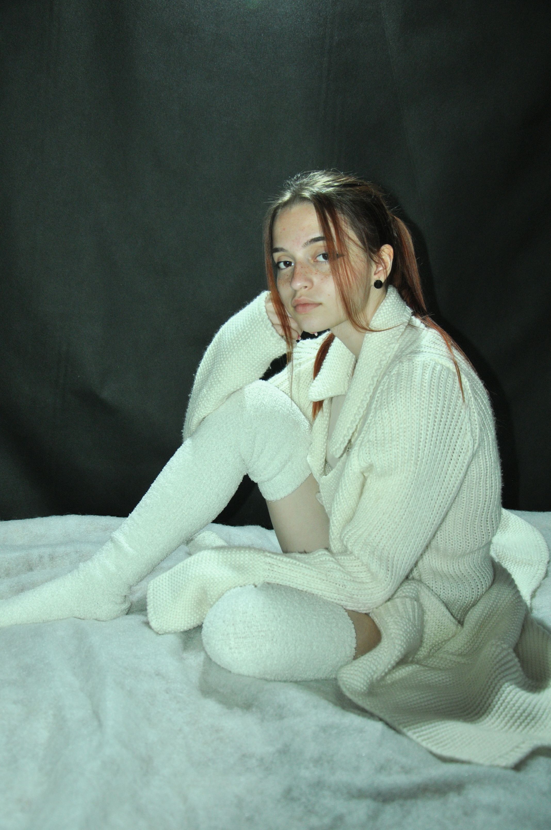 Portrait of a woman in white knitwear sitting on a bed, exuding warmth and coziness.