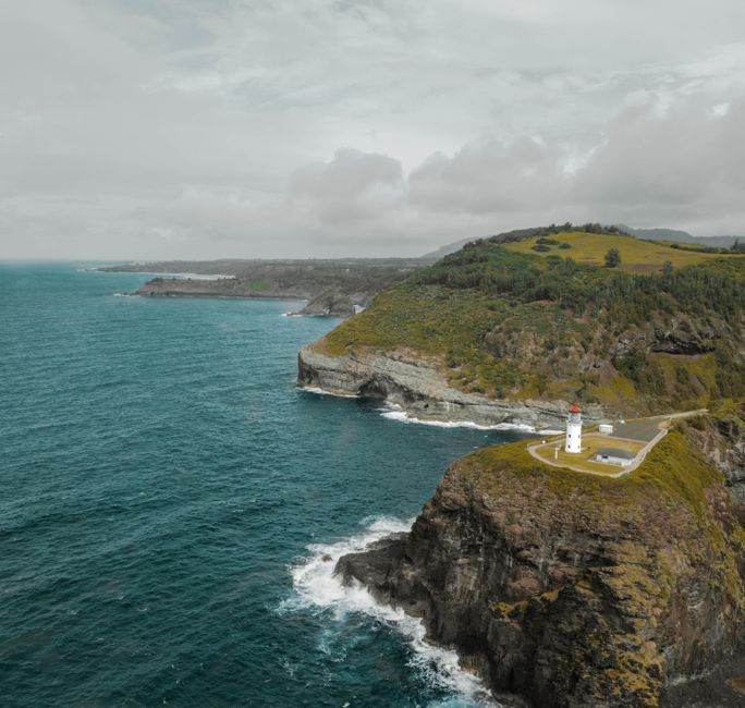 A picturesque lighthouse perched on a cliff by the ocean, surrounded by lush greenery and dramatic sea views.