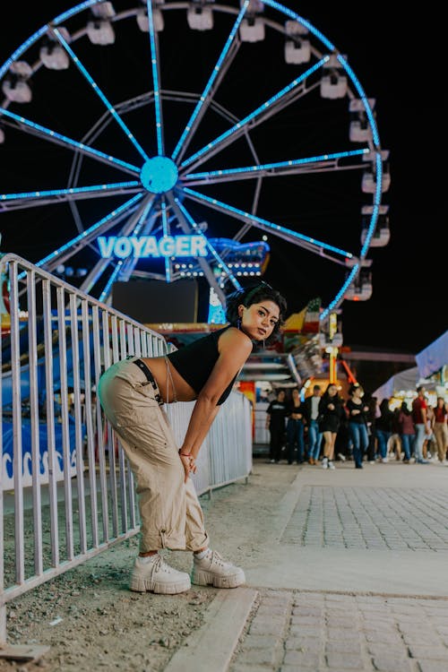 Model in a Black Crop Top and Beige Pants Posing in Front of a Ferris Wheel
