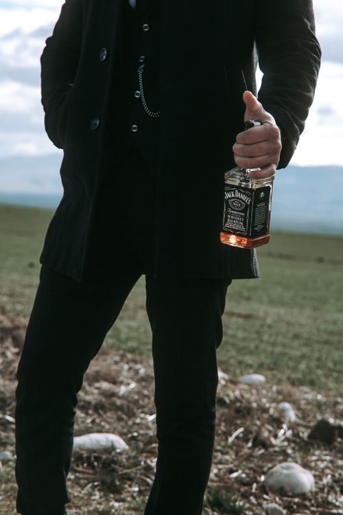 Free A man in a coat holding a Jack Daniel's bottle in a natural outdoor setting. Stock Photo