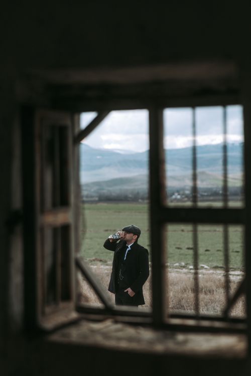 Free Well-dressed man drinking whiskey outdoors, viewed through rustic window. Stock Photo