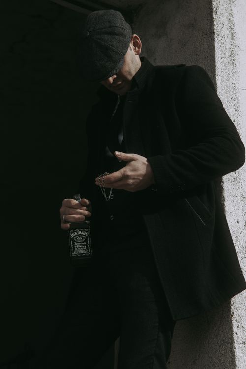 Free A man in a black coat and cap holding a Jack Daniels bottle, exuding elegance and mystery. Stock Photo