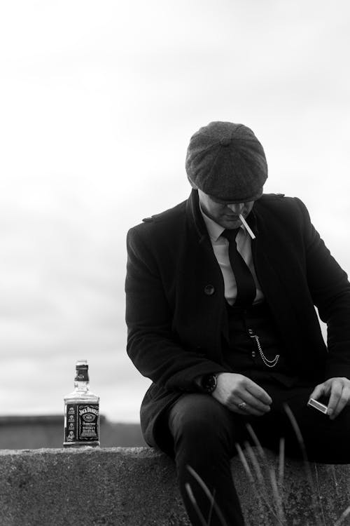 Free Man Wearing a Flat Cap Smoking a Cigarette Next to an Opened Bottle of Jack Daniels Stock Photo