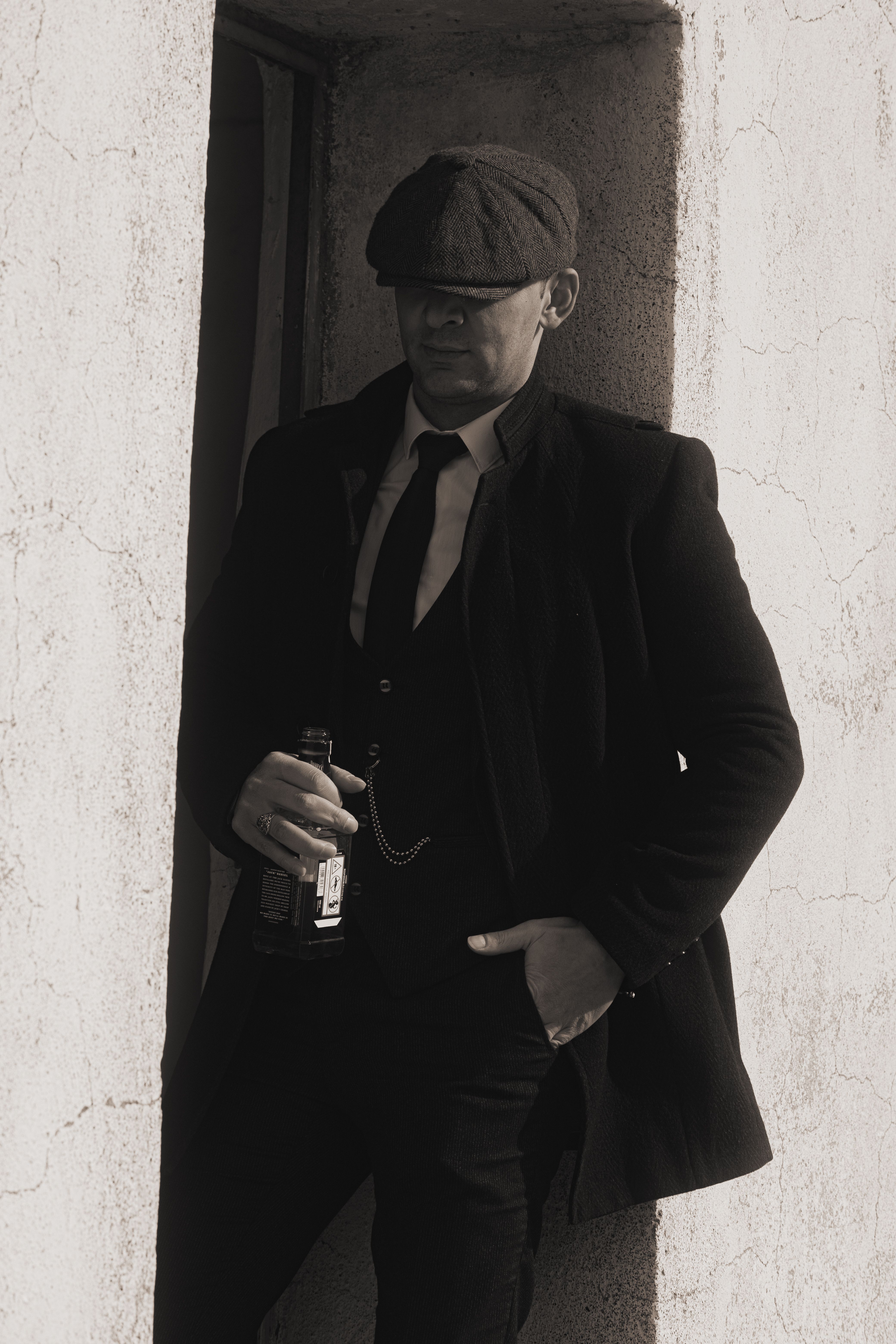 A man in a suit and hat leans against a wall holding a bottle. Vintage and elegant style.