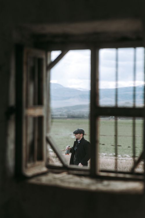 Free View of a man holding a bottle in a rural landscape, captured through a rustic window for a vintage feel. Stock Photo
