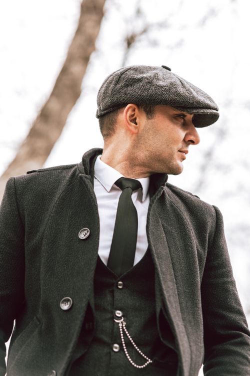 Free Fashionable man wearing a suit, coat, and ivy cap, posing stylishly outdoors. Elegant and sophisticated look. Stock Photo