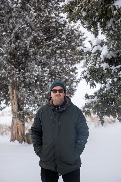 Free Man in a winter jacket standing in snow-covered forest with trees in the background. Stock Photo