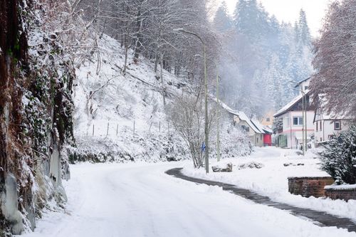 Free Scenic view of a snowy village road nestled between hills and trees in winter. Stock Photo