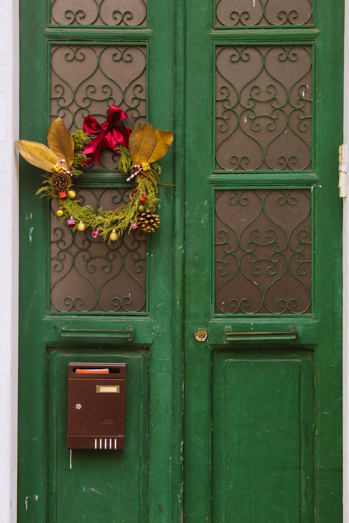 Green apartment front door with a small autumn-toned Christmas wreath and a red mailbox