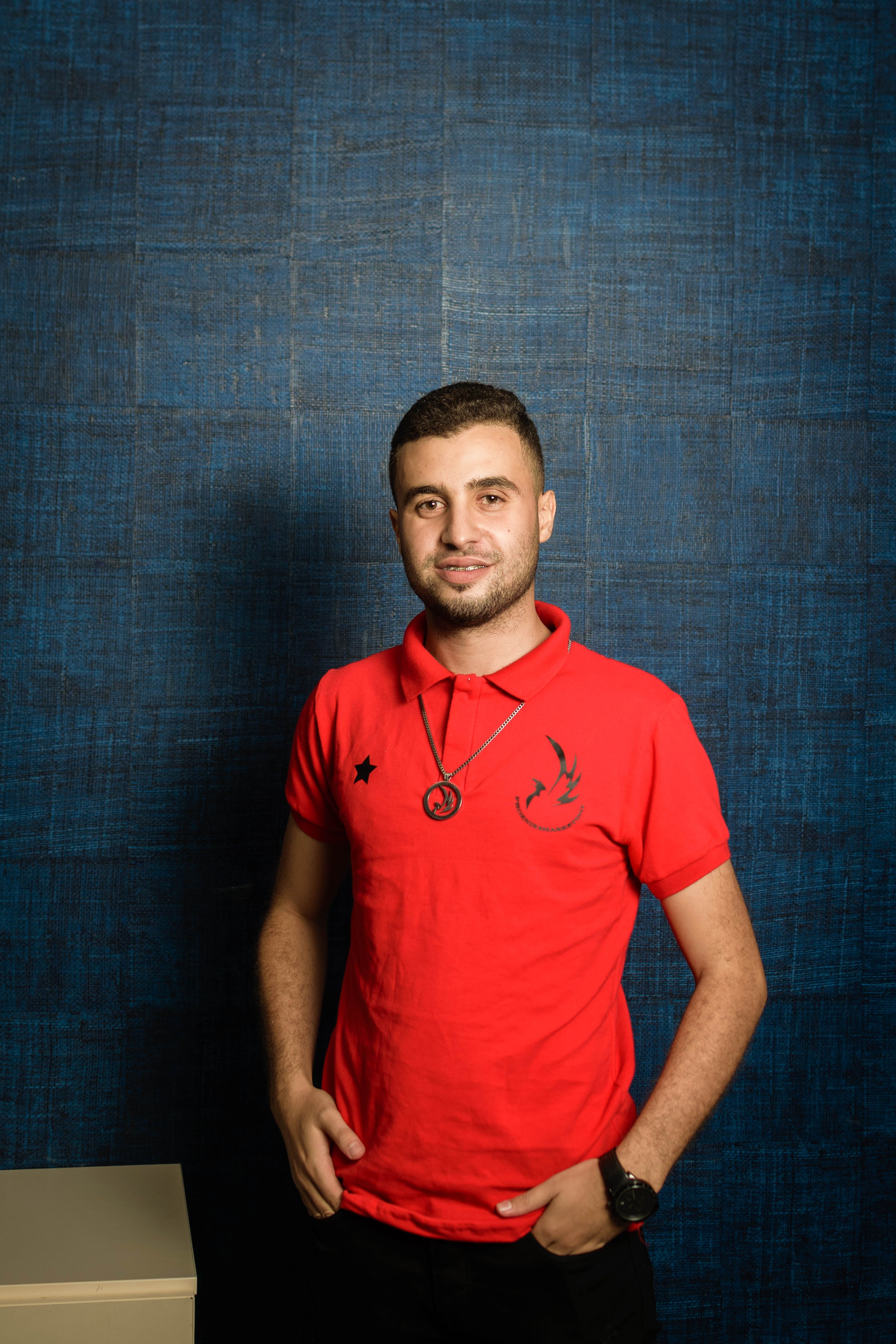 A young man in a red polo shirt posing confidently with a pendant and watch.