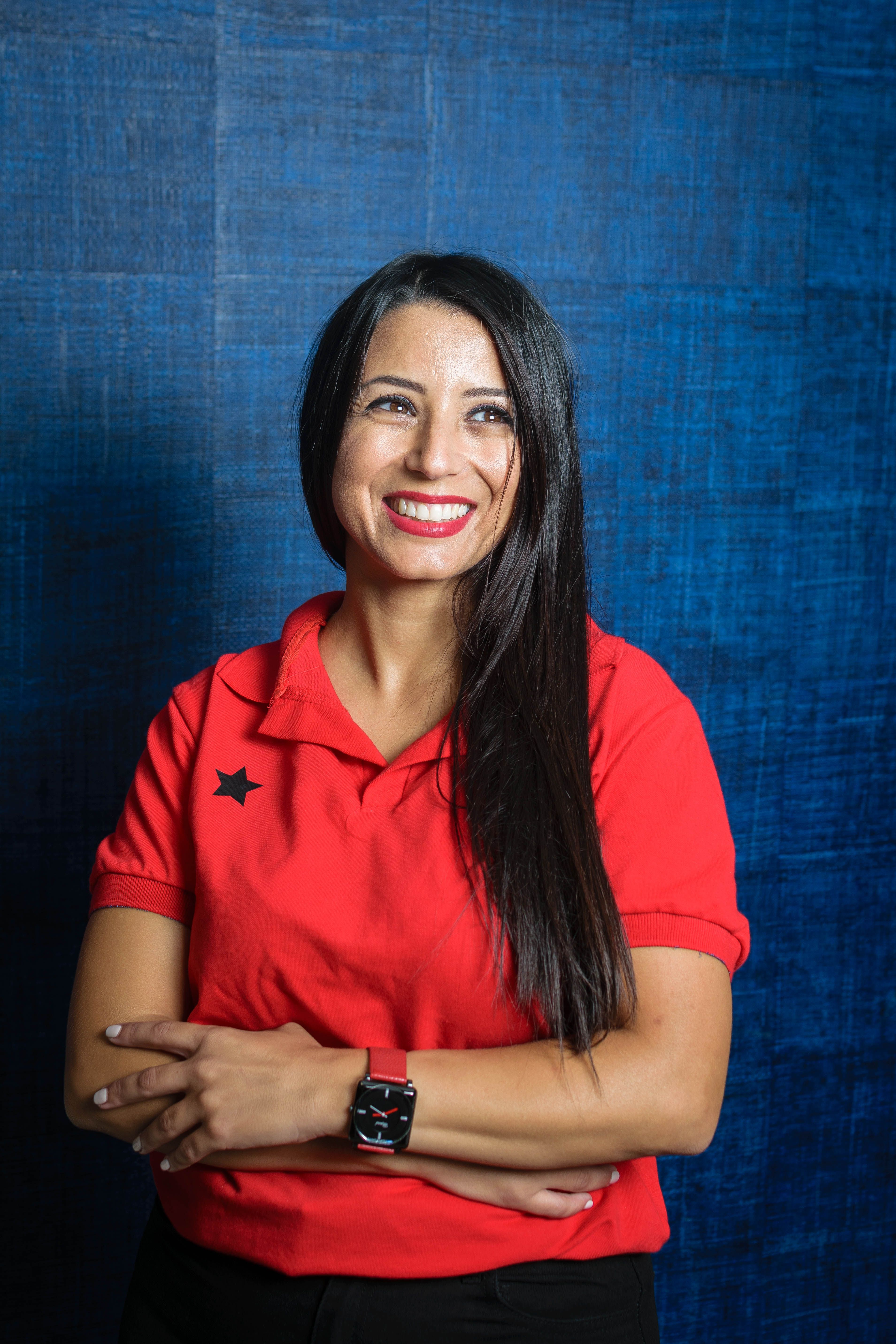 A cheerful young woman in a red shirt smiles warmly against a textured blue background.