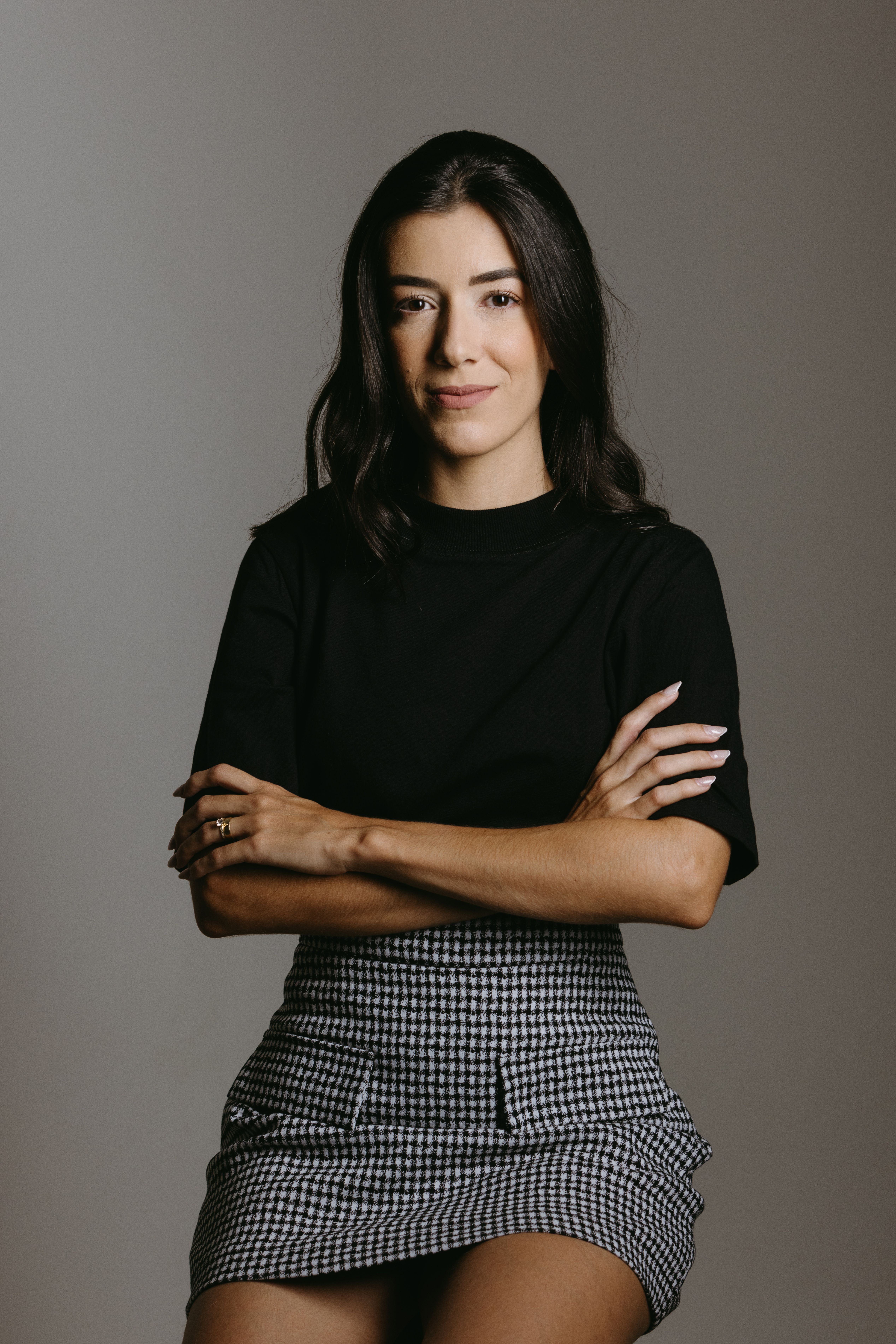 Studio portrait of a stylish young woman in a black top and skirt, arms crossed, smiling confidently.