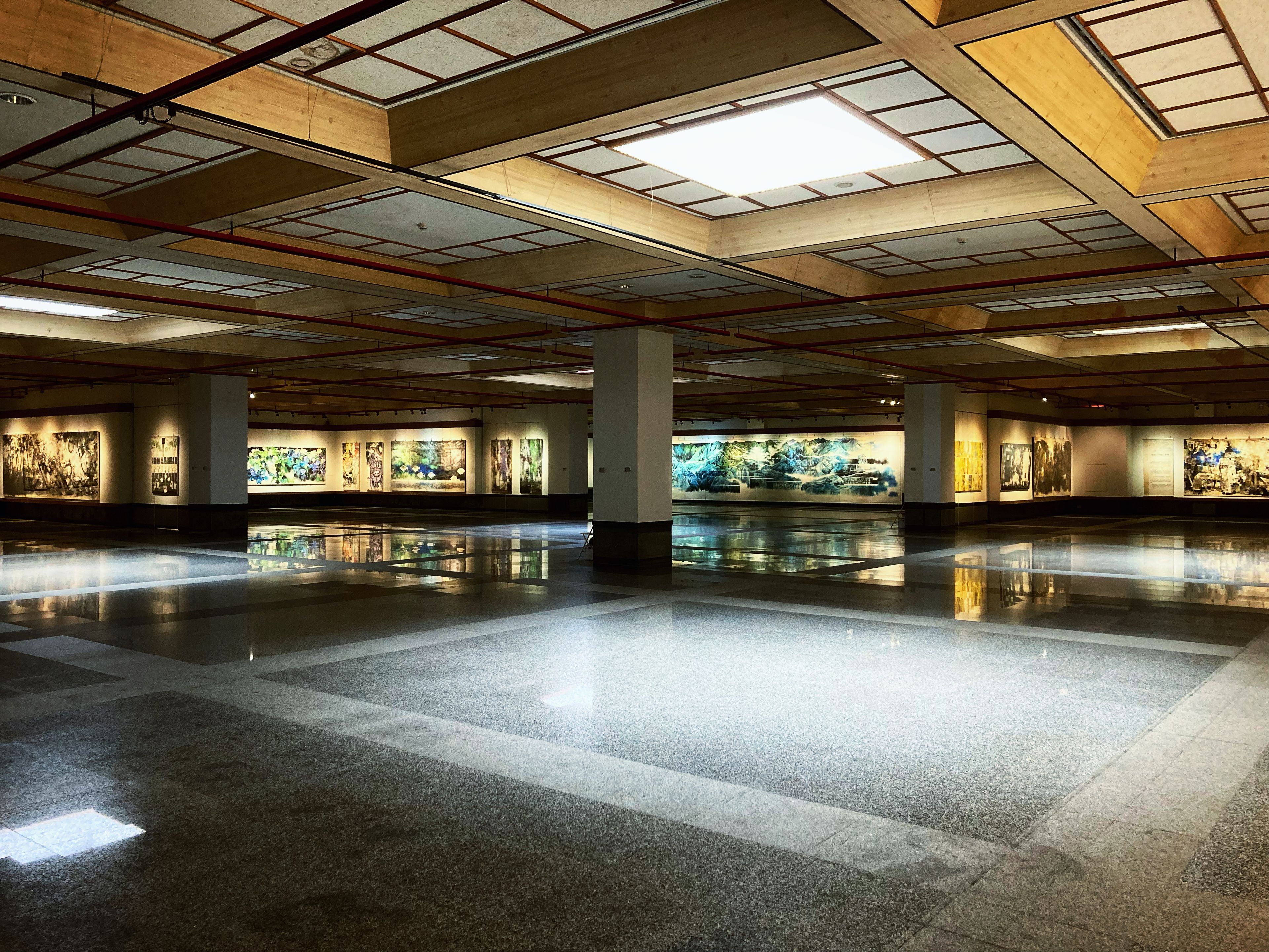 A large, empty art gallery showcasing modern paintings under bright indoor lighting.