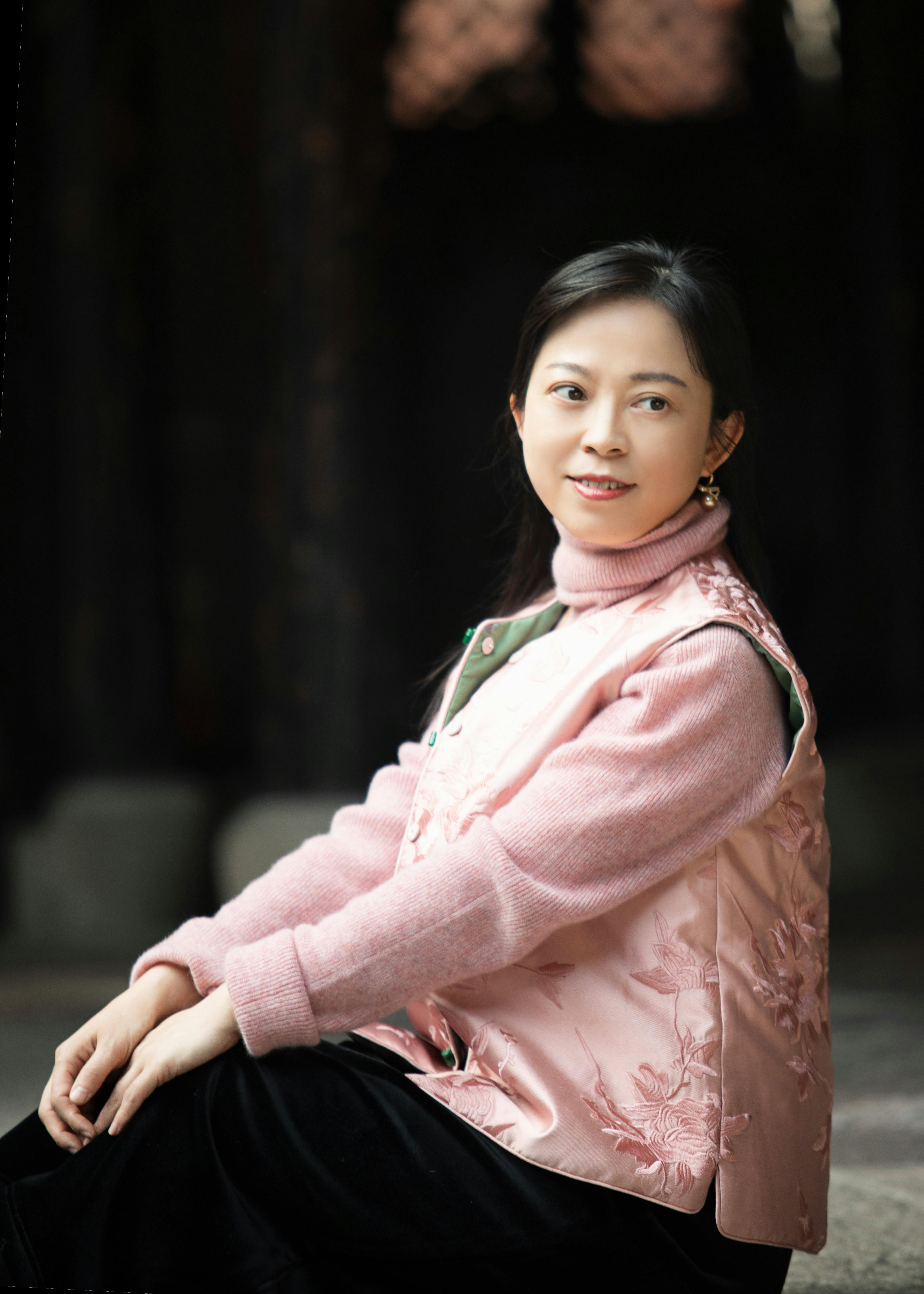 Portrait of a woman sitting in a pink sweater and vest, exuding elegance indoors.