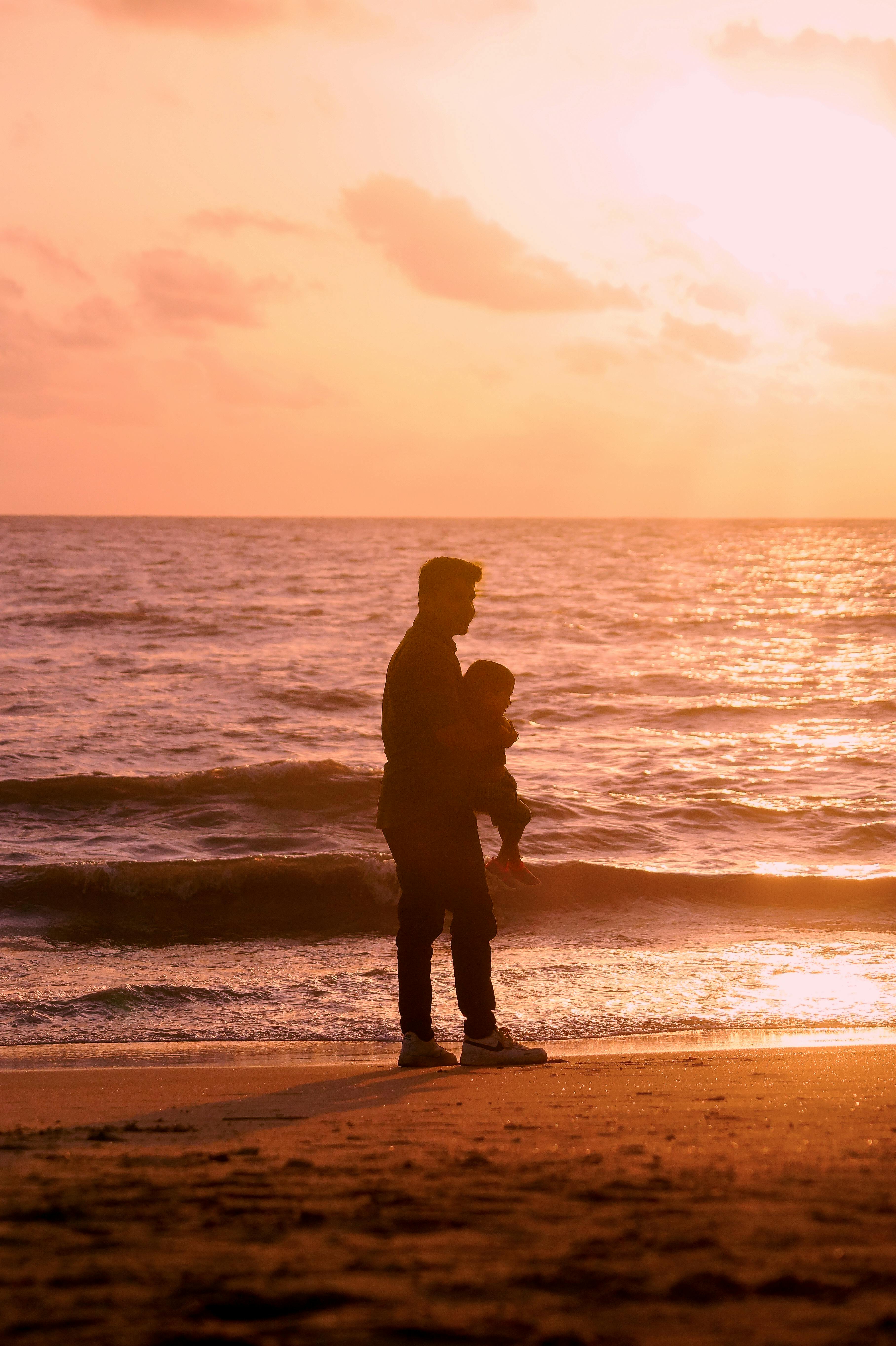 A touching silhouette of a father holding his child by the sea at sunset.