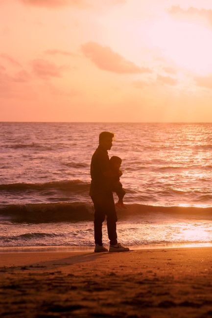 A touching silhouette of a father holding his child by the sea at sunset.