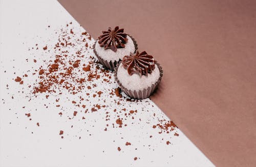 Two cupcakes on a brown surface with sprinkles