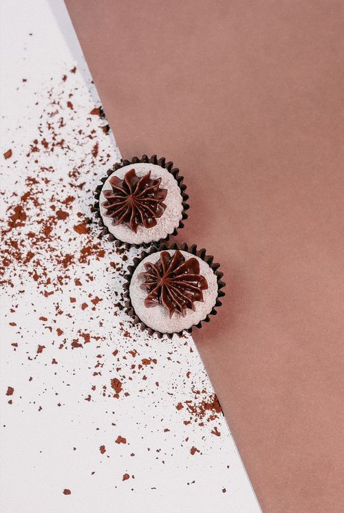 Free Two chocolate cupcakes with creamy frosting, dusted with cocoa powder, on a brown and white background. Stock Photo