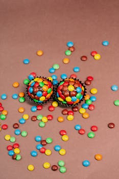 Eye-catching cupcakes covered with a variety of colorful candies scattered over a brown background in a studio setting.