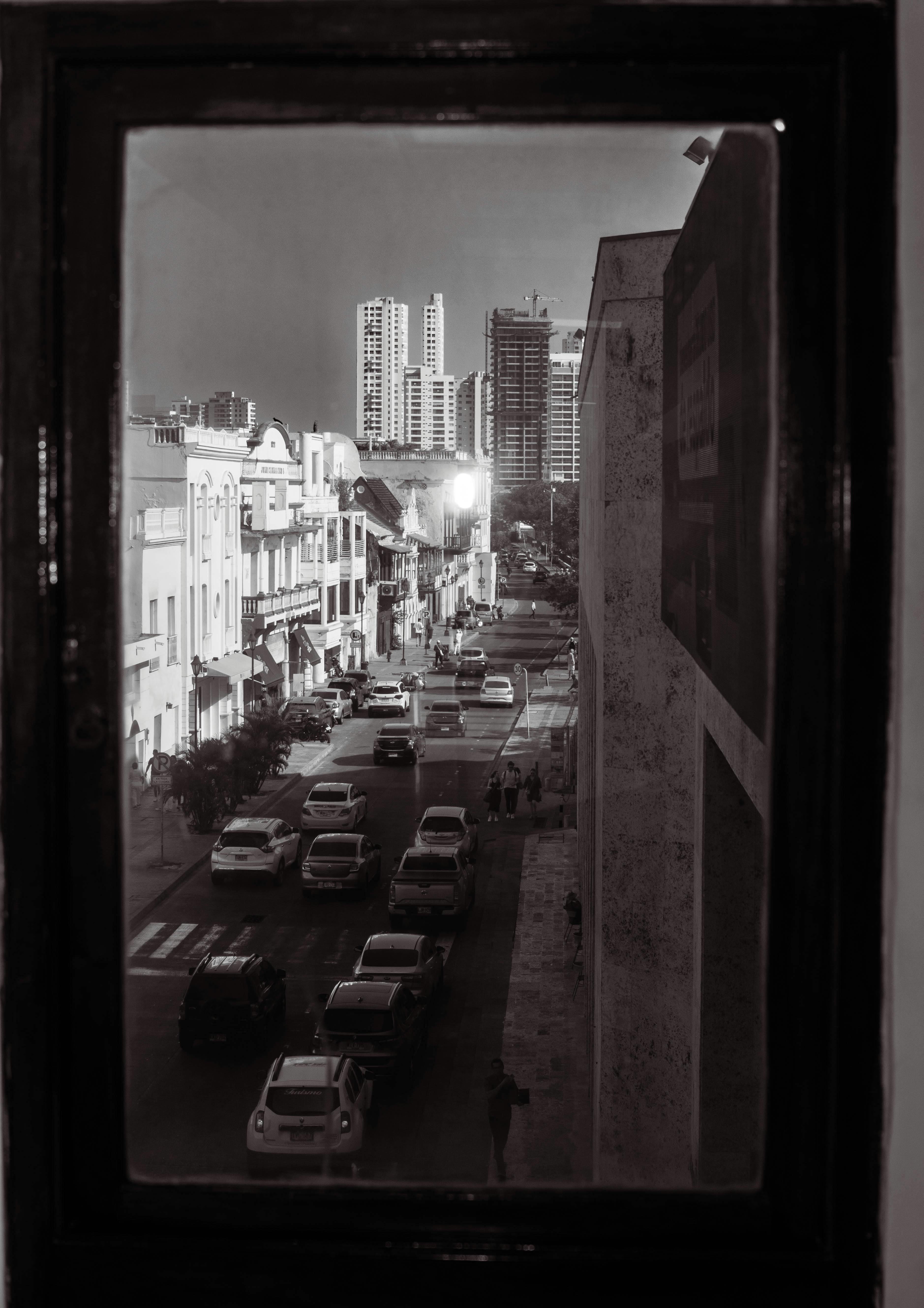 black and white photo of a busy street in city seen through the window