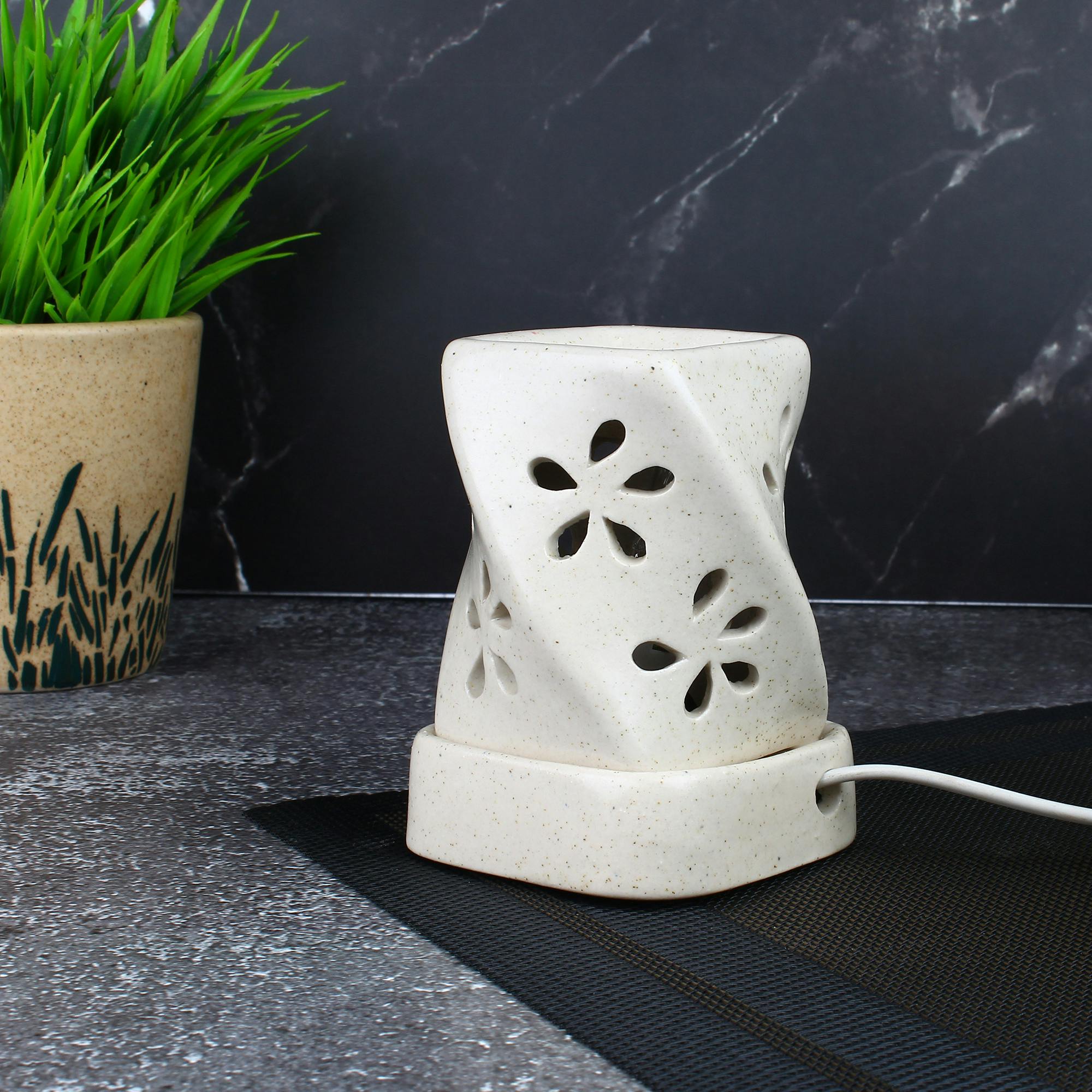 Close-up of a ceramic diffuser with floral cutouts, next to a potted plant on a marble surface.