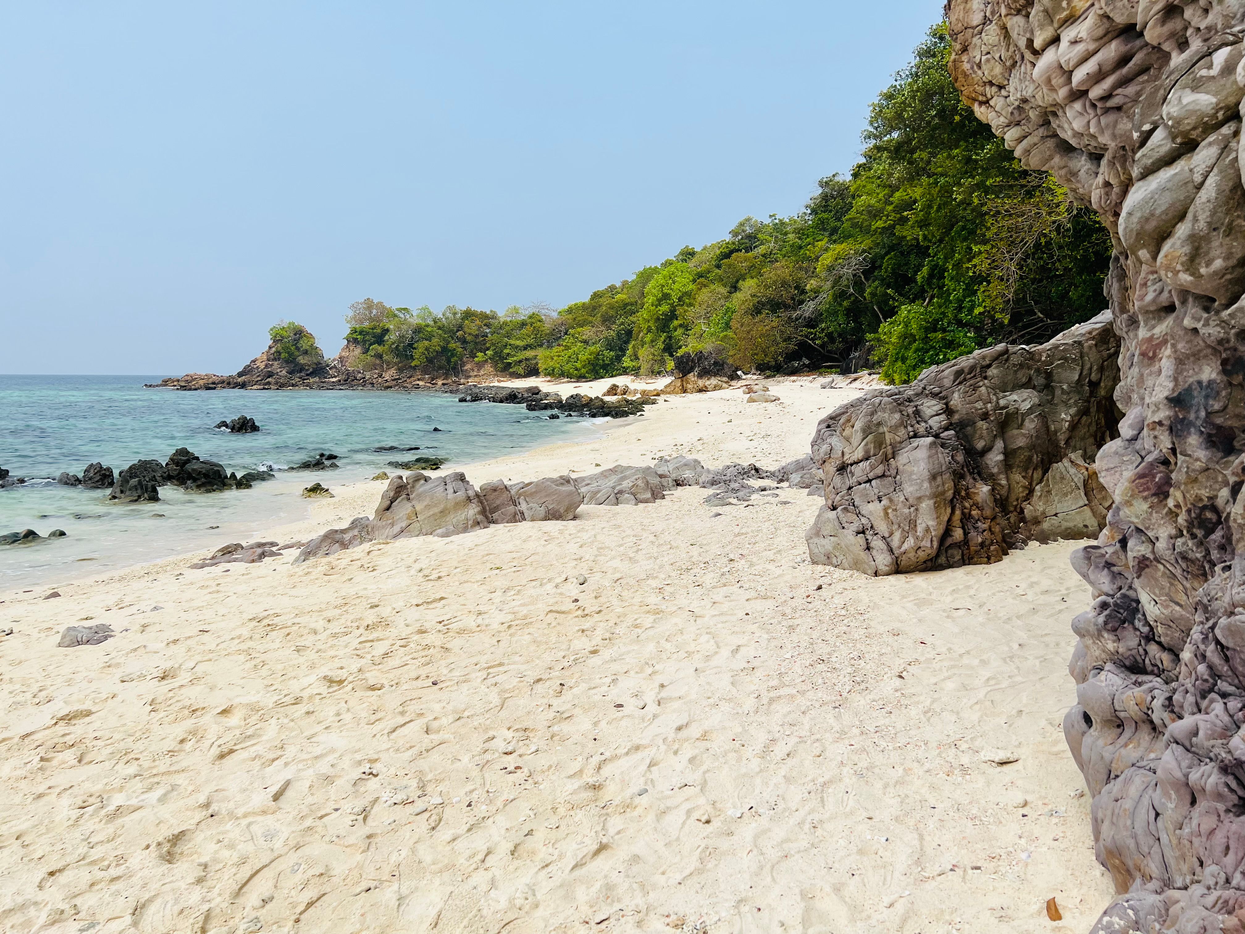 Beautiful sandy beach with rocky cliffs and lush greenery in Ko Tarutao, Thailand.