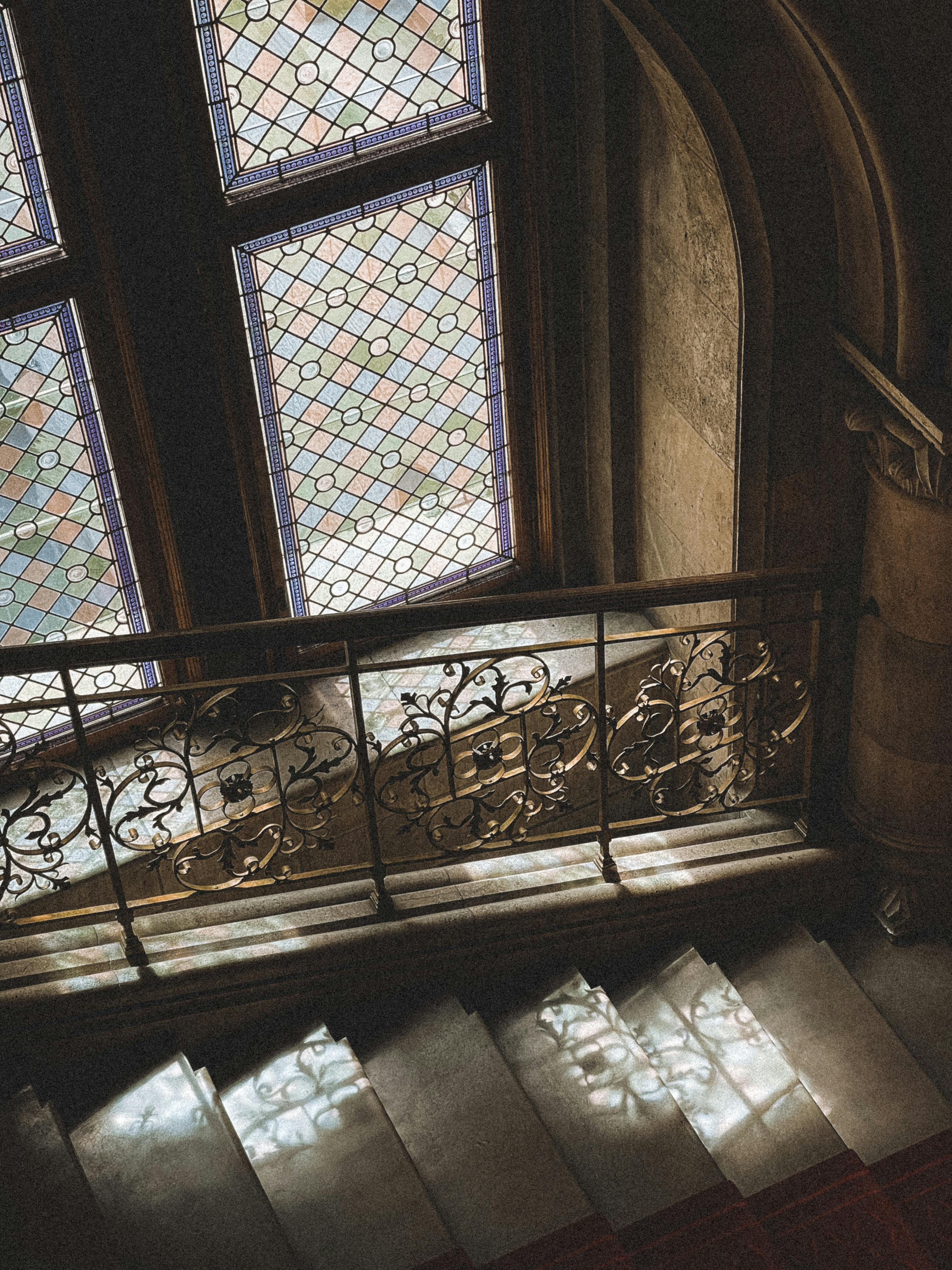 A beautifully ornate staircase with stained glass windows casting colorful light in a historical Vienna building.