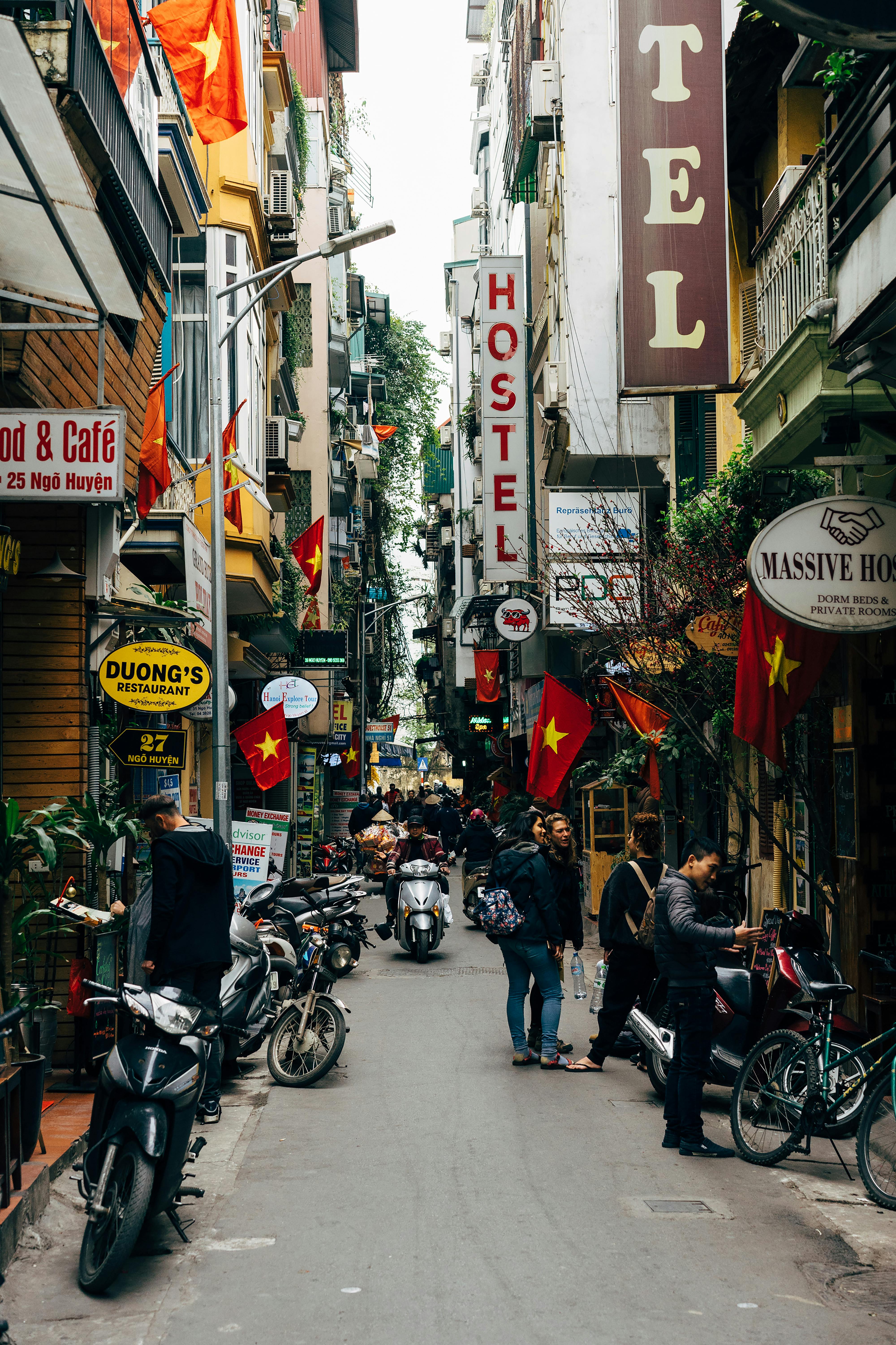 Bustling Hanoi street with hostels, scooters, and vibrant culture, typical of Southeast Asian urban life.