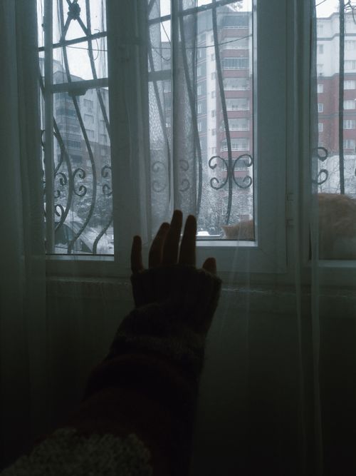 Free A hand reaches through sheer curtains towards a snowy urban landscape from an apartment window. Stock Photo