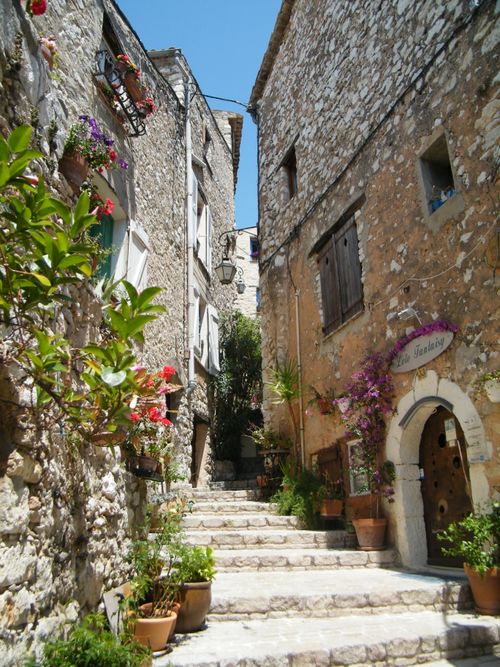 Free A picturesque stone alley with stairs, vibrant flowers, and rustic walls under a clear blue sky. Stock Photo