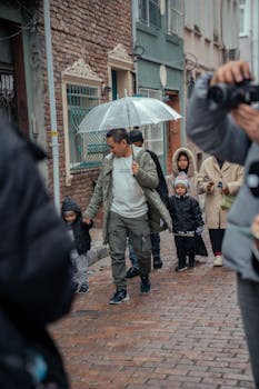A family walking through a cobblestone city street during rainy weather, holding an umbrella.