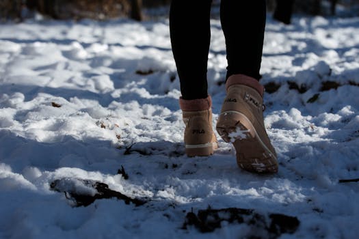 Person walking in brown boots on a snow-covered forest path, captured from behind.