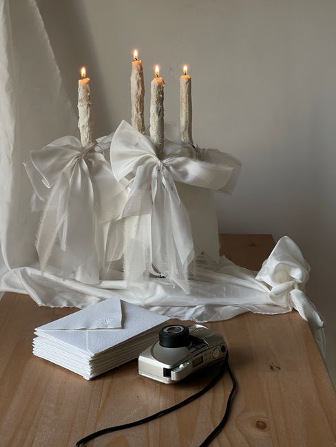 Captivating setup with lit candles, white bows, and a vintage camera on wooden table.