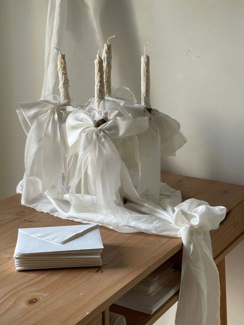 Styled wooden table with white candles, fabric, and envelopes for a classic ambiance.