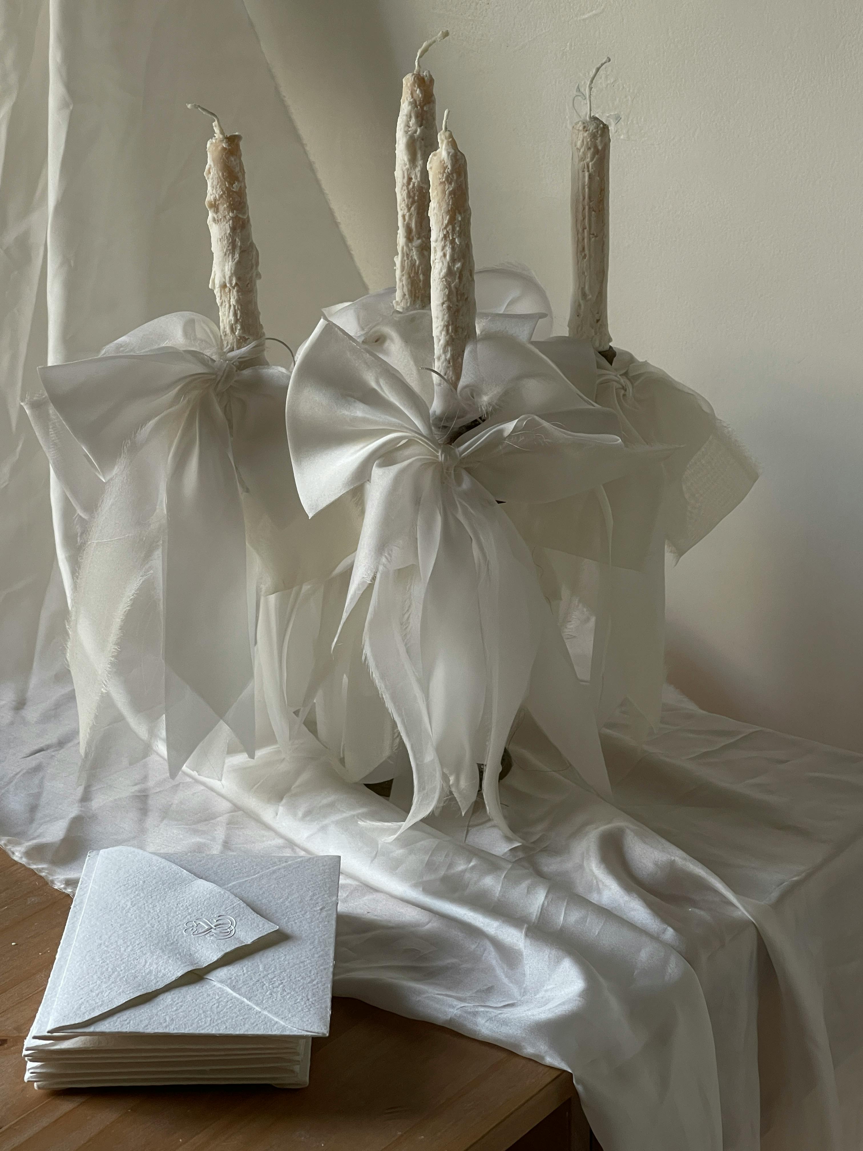 Minimalist decor featuring white ribbons, wax candles, and envelopes on a table.