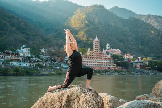 A woman performs a yoga pose by the riverbank near Tera Manzil Temple in Rishikesh, India.