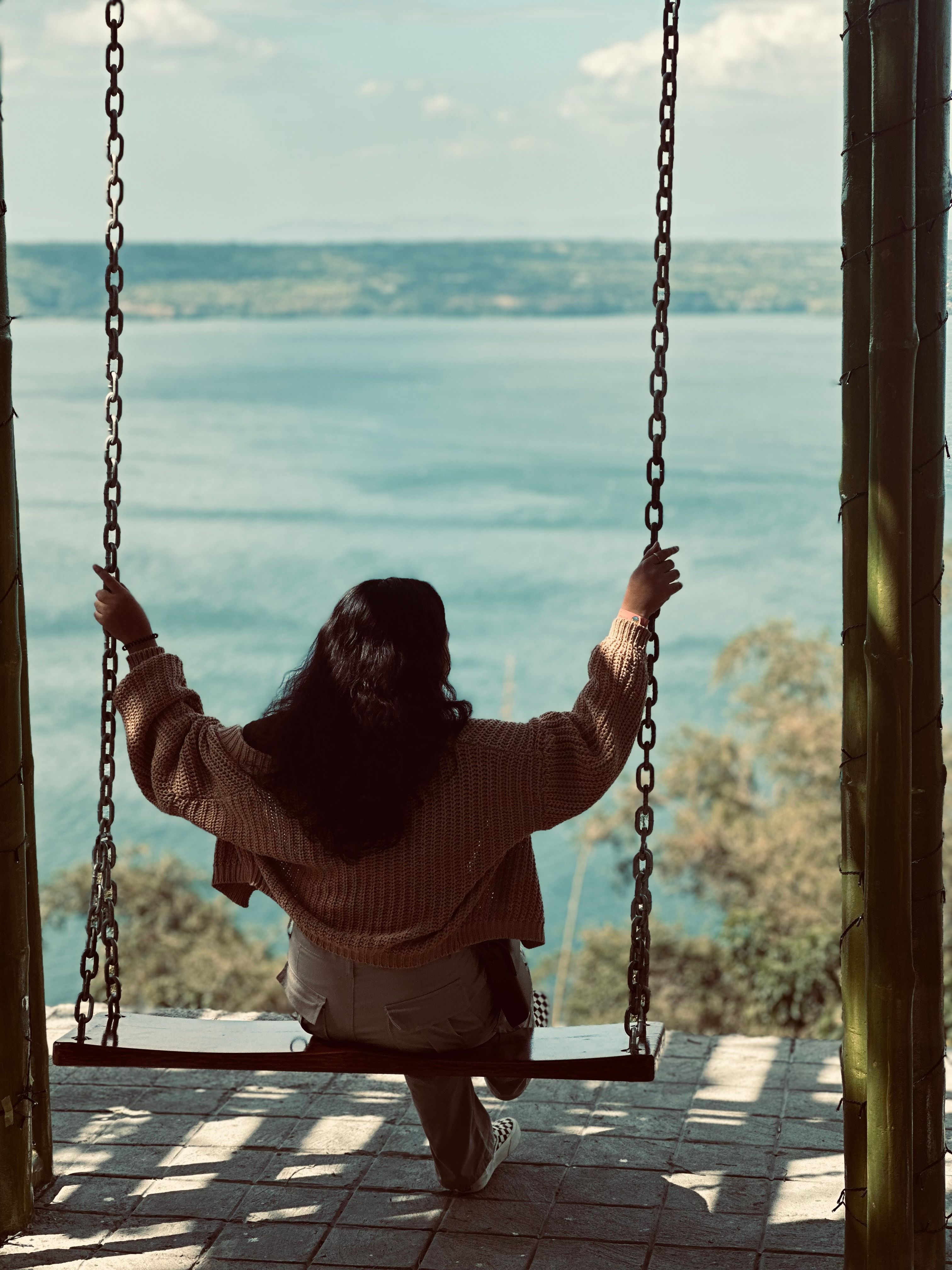 A woman sitting on a swing looking out over the water · Free Stock Photo