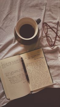 Flat lay of coffee, open notebook, pen, and eyeglasses on a fabric surface.