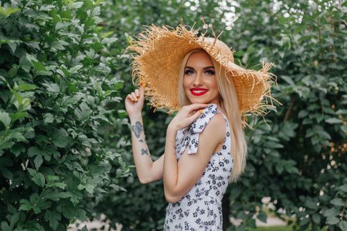 Free Charming blonde woman in a straw hat smiling outdoors in a floral sundress. Stock Photo