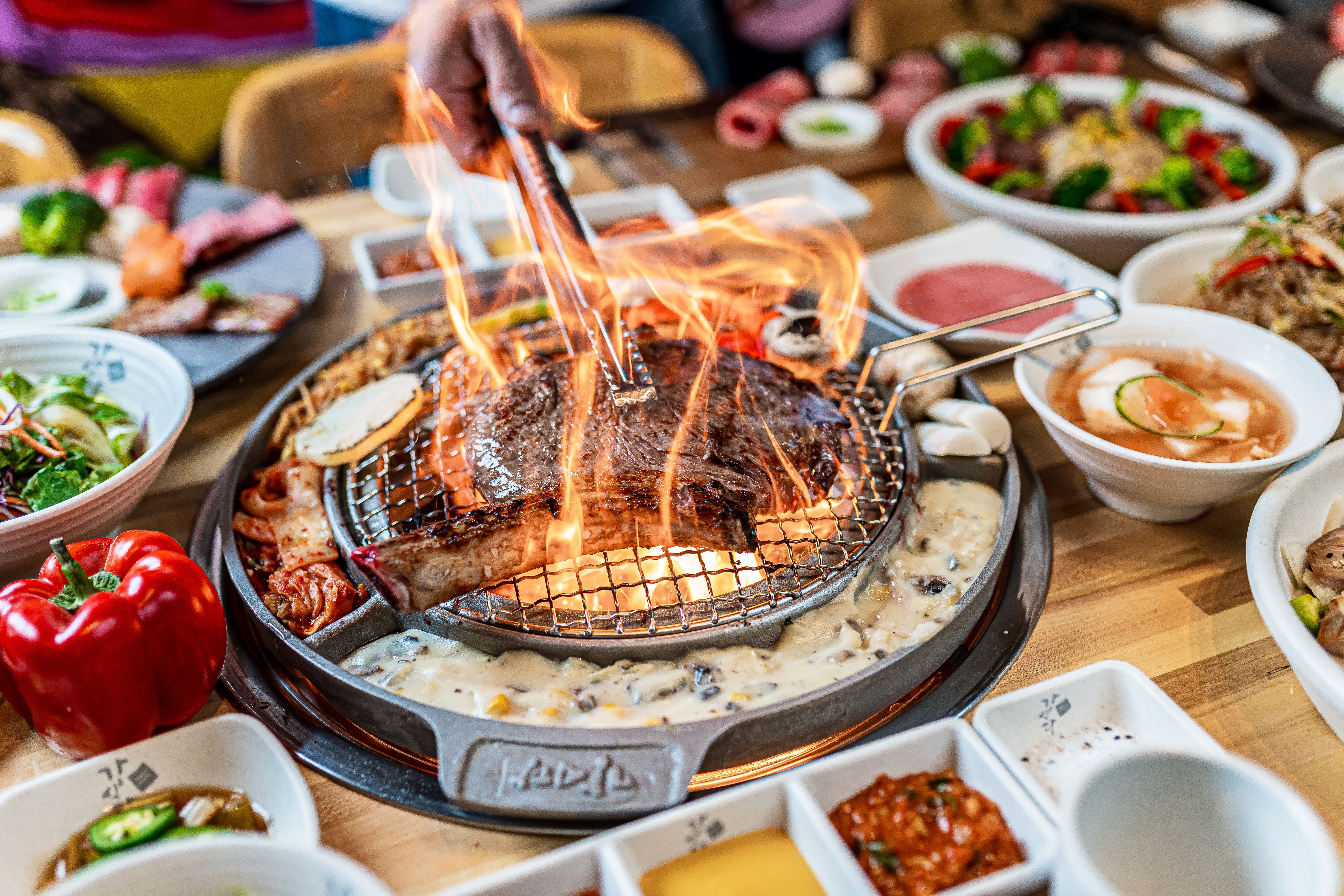 A diverse group of friends smiling and cooking meat on a grill at a lively Korean BBQ restaurant.