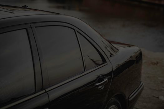 Close-up of a black car's side view with tinted windows by a calm riverbank.