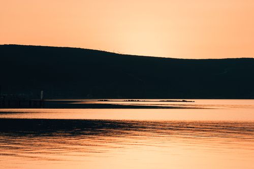 Free Golden sunset reflecting on calm waters, silhouetting distant hills and wind turbines. Stock Photo