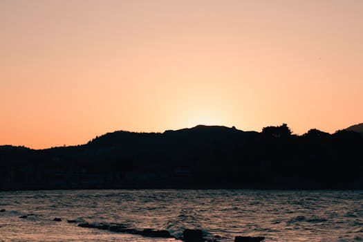 Peaceful ocean view with mountains silhouetted against a vivid sunset sky.