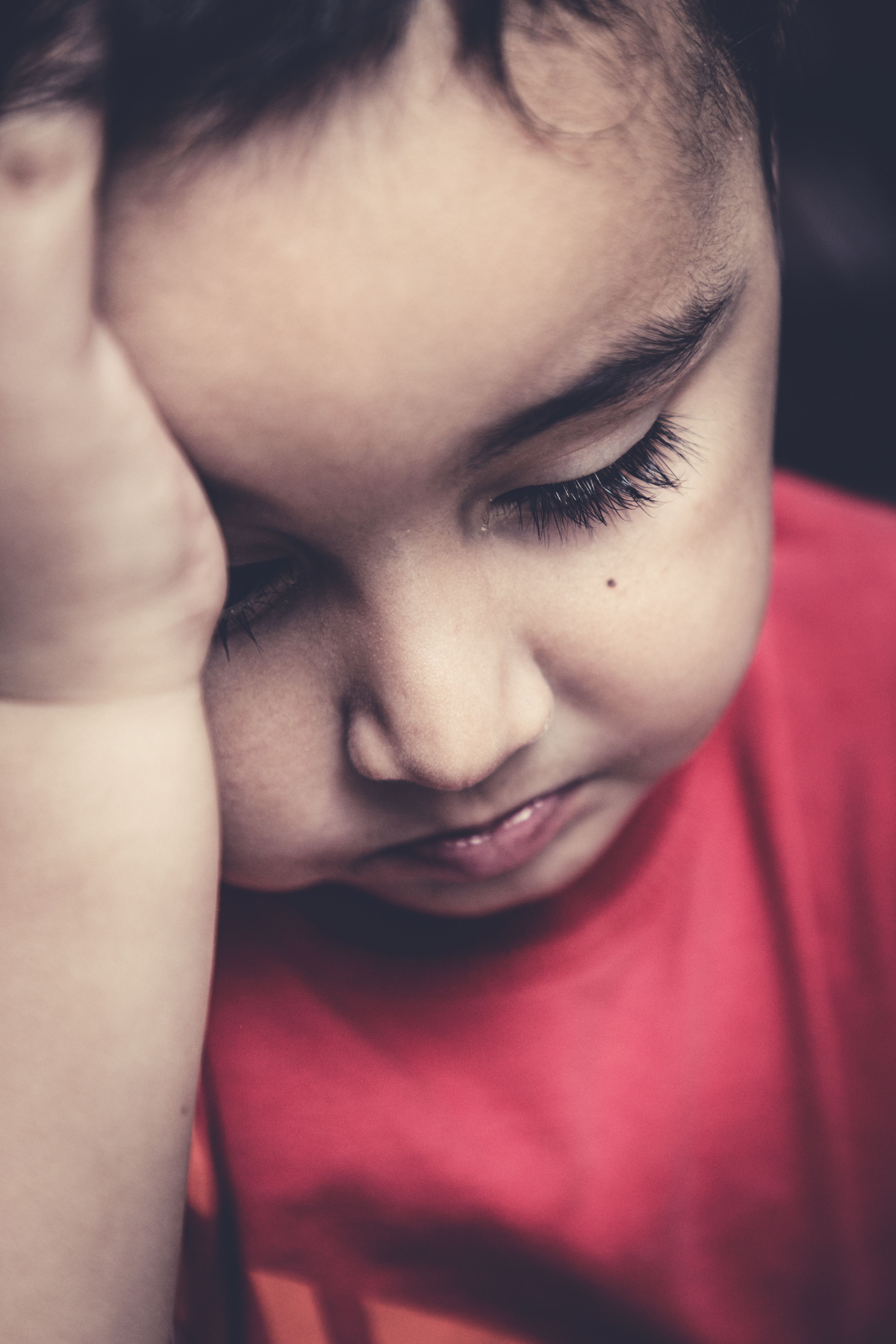 Primo piano di un bambino piccolo triste, con la fronte poggiata contro il palmo della mano.
