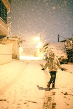 A young girl plays joyfully on a snowy street at night, surrounded by falling snowflakes.