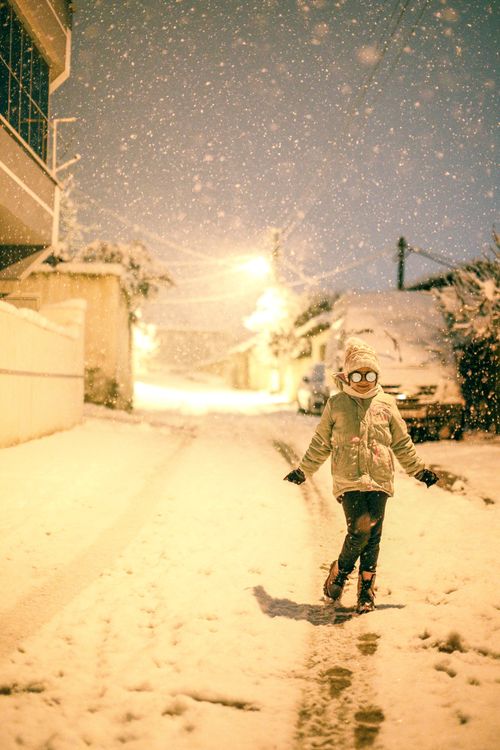 Free A young girl plays joyfully on a snowy street at night, surrounded by falling snowflakes. Stock Photo