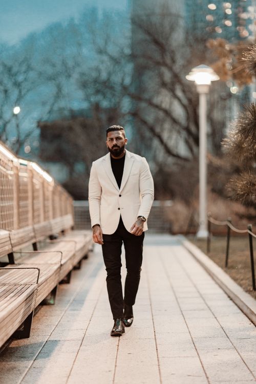 Free Sophisticated man in white suit walks down a well-lit urban park pathway at dusk. Stock Photo